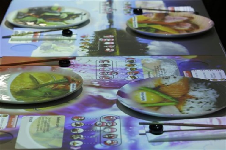 The interactive menu is projected onto the table and dishes are seen in an Inamo restaurant in central London, Monday, July 4, 2011. Want a virtual bite of what you'll eat before ordering from the menu?  An Asian-themed restaurant in London's theater district is giving its customers just that, projecting images of dragon rolls, black cod, and other dishes directly onto diners' plates.  (AP Photo/Sang Tan)